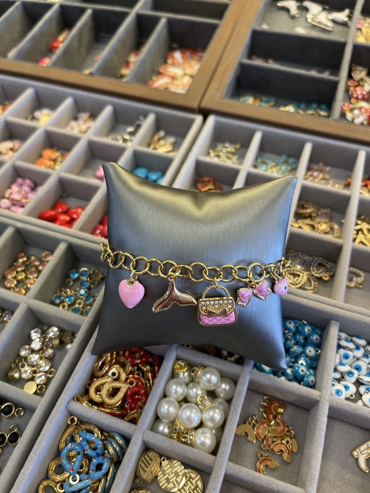 Finished charm bracelet on a display pillow over trays of charms