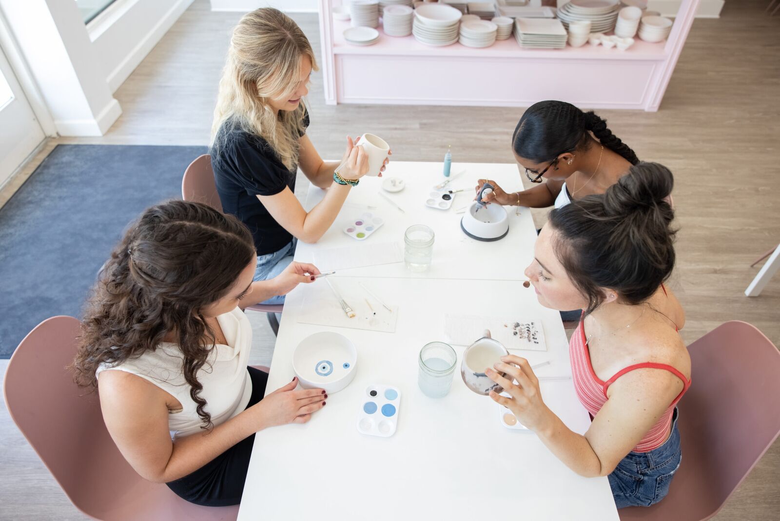 Four friends painting mugs and bowls around a studio table