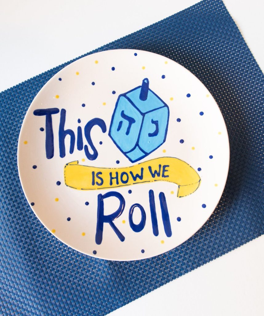 Hand-painted Hanukkah plate with a blue dreidel and the words This Is How We Roll