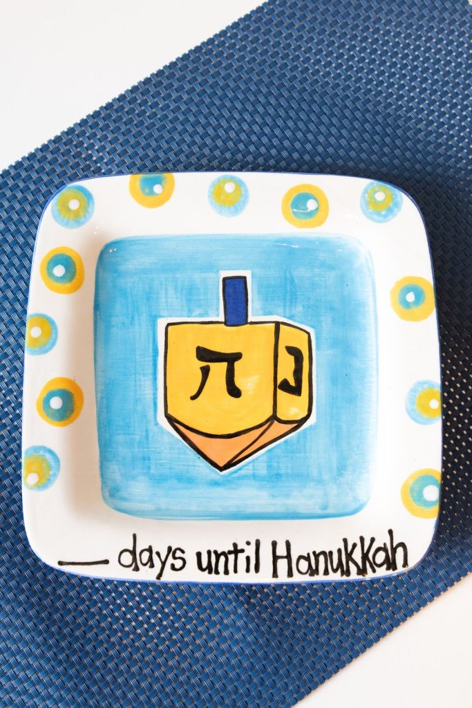 Square Hanukkah plate with a yellow dreidel on blue and the words days until Hanukkah