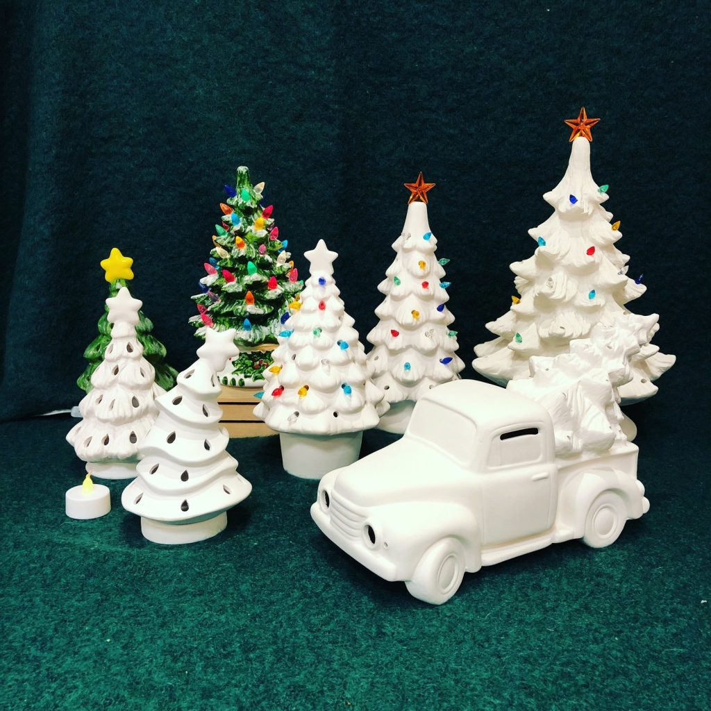 Ceramic Christmas trees with colored bulbs and an unpainted white pickup truck on a dark green backdrop