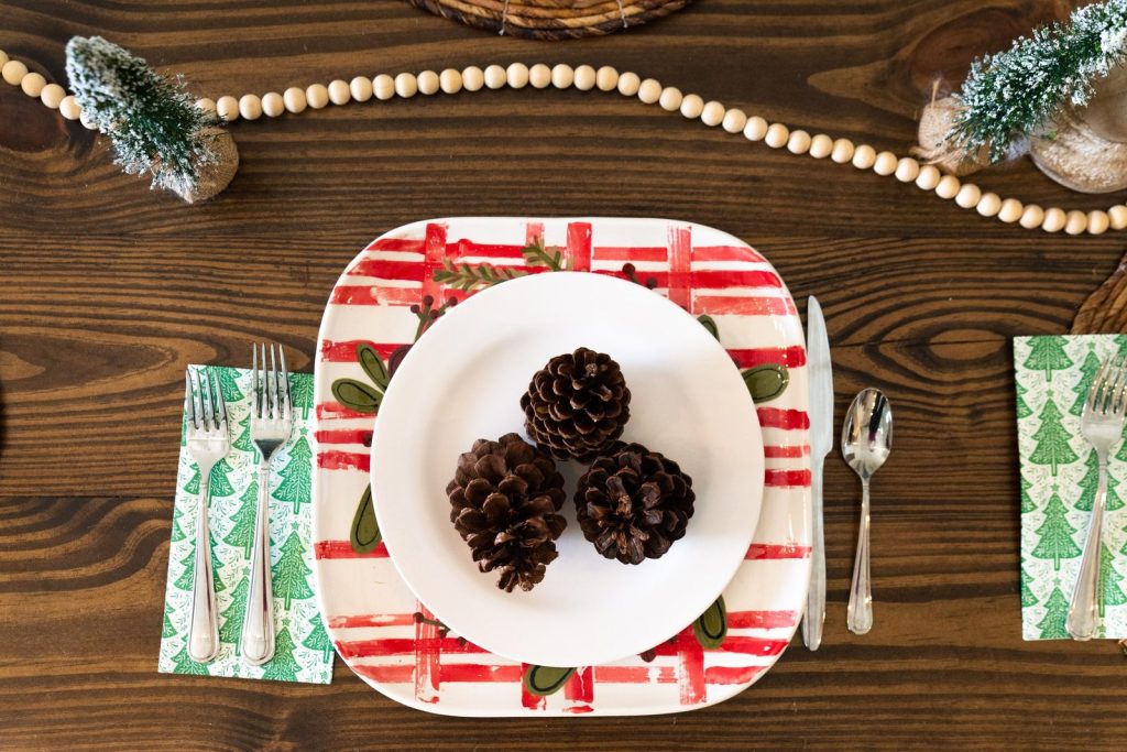Hand-painted square charger with red and green stripes holding a plate of pinecones on a holiday table