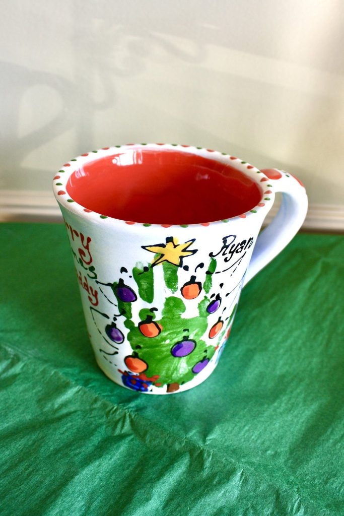Hand-painted mug with a green handprint Christmas tree and colorful ornaments and a red interior