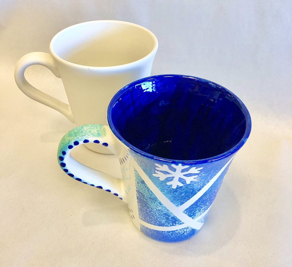 Hand-painted cobalt blue mug with a white snowflake beside an unpainted white mug