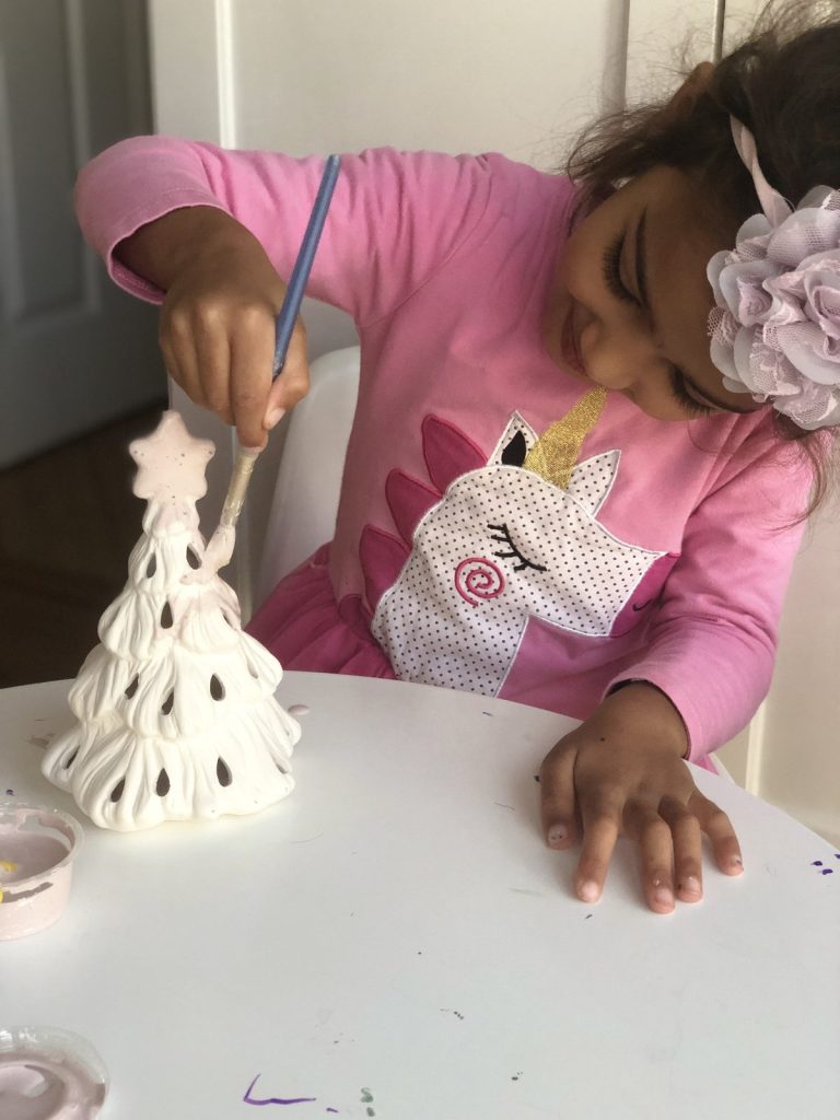 Young girl in pink painting a small white bisque Christmas tree with a brush