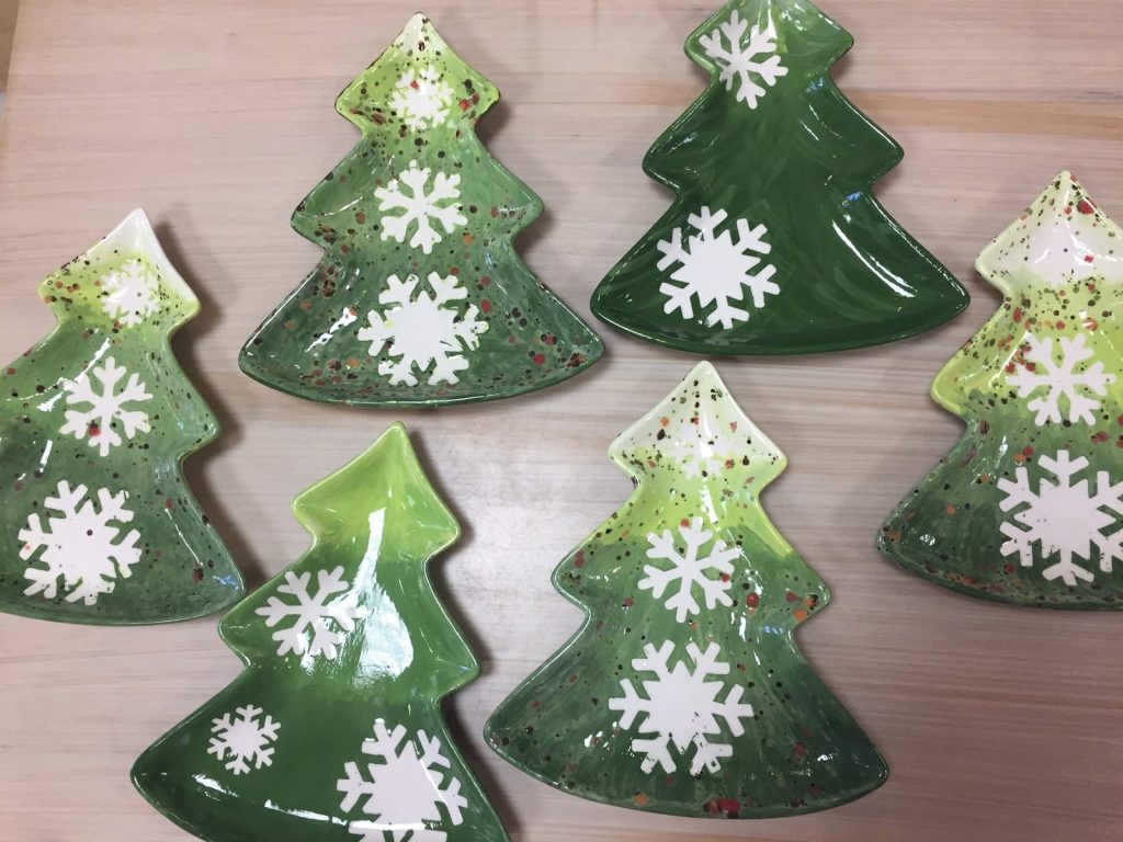 Several hand-painted Christmas tree-shaped dishes in shades of green with white snowflakes