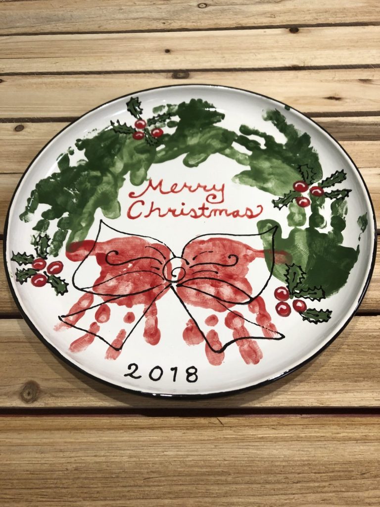 Hand-painted Merry Christmas platter with a green handprint wreath and red handprint bow, dated 2018