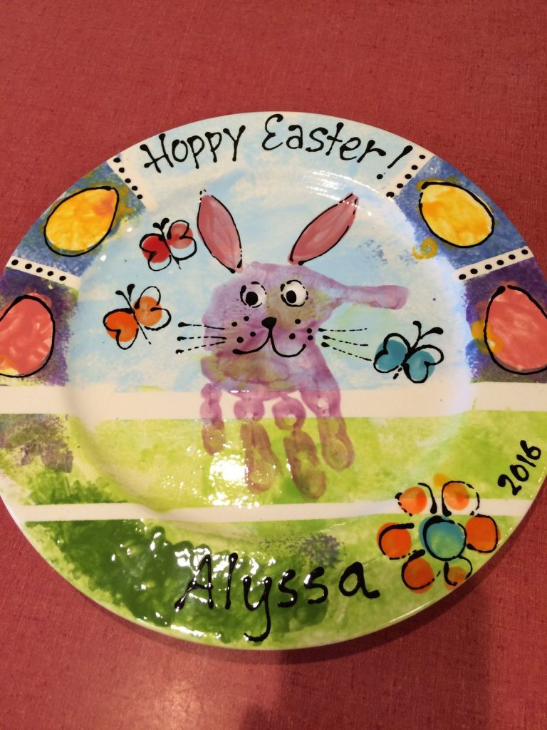 Hand-painted Easter plate with a purple handprint bunny, butterflies, painted eggs and a green grass border