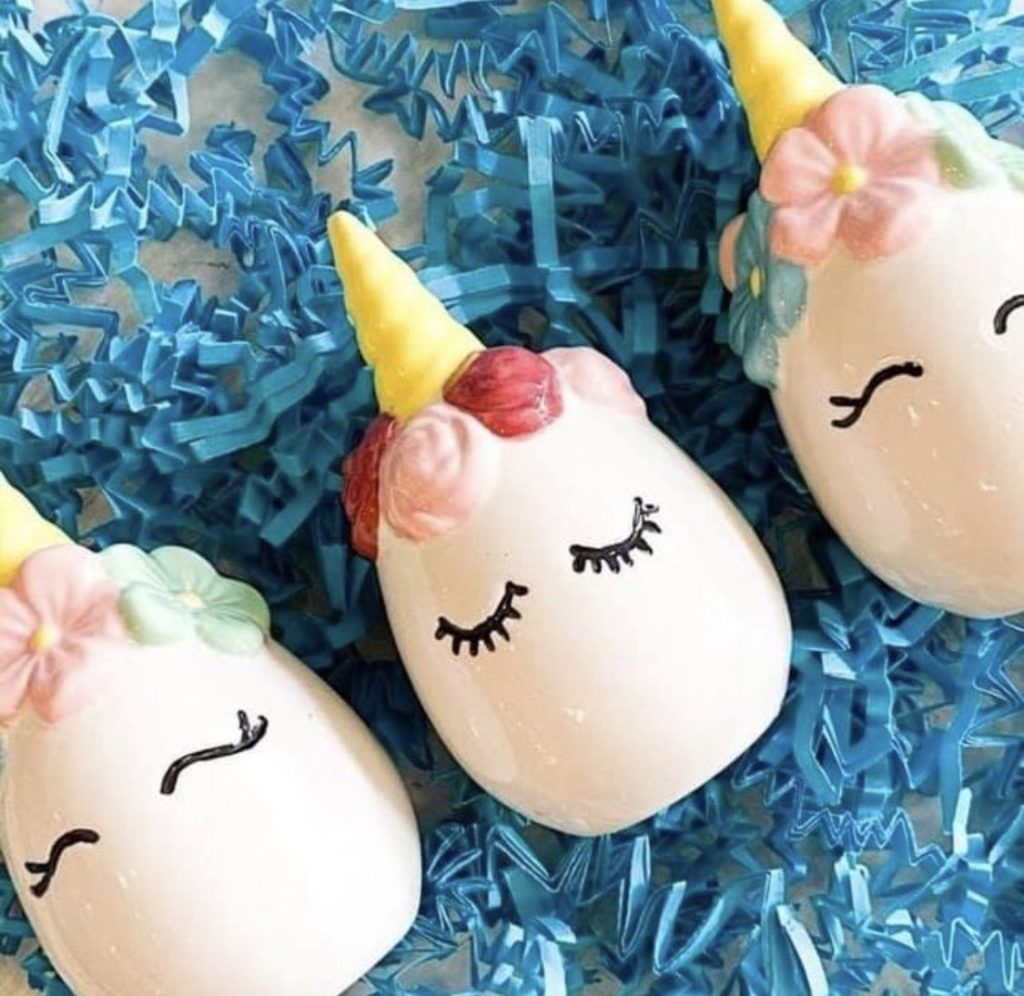 Three white hand-painted ceramic unicorn eggs with sleepy eyes, flower crowns and yellow horns