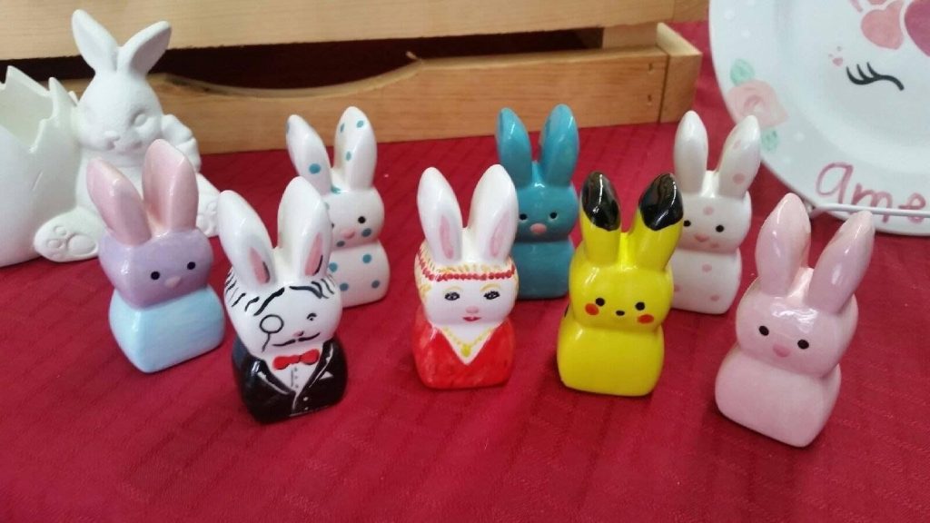 Row of hand-painted ceramic bunny figurines in pastels, a tuxedo and teal, on red cloth
