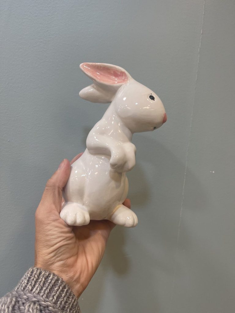 Hand holding a glossy white ceramic bunny figurine with pink ears