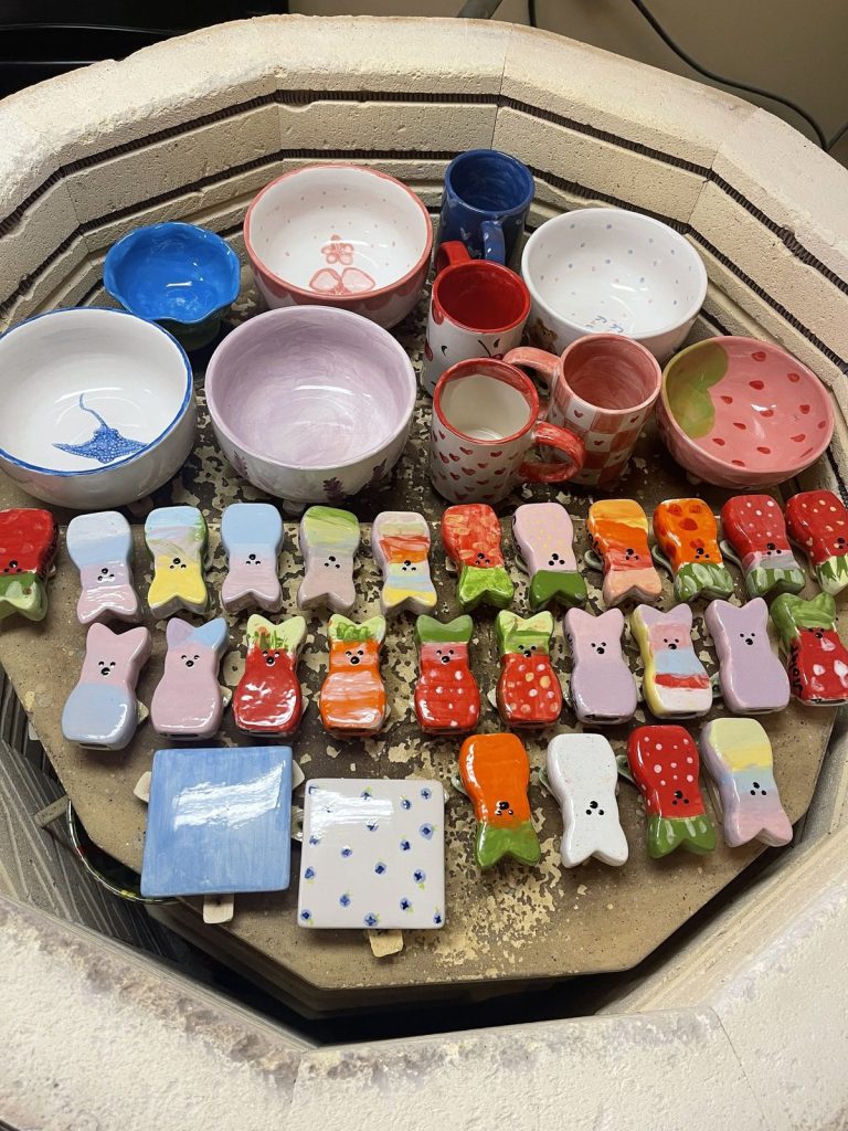 Freshly glazed bowls, mugs, tiles and colorful bunny figurines loaded inside an open kiln