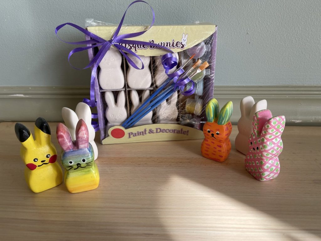 Hand-painted bunny figurines in yellow, rainbow, orange and pink beside a boxed paint kit
