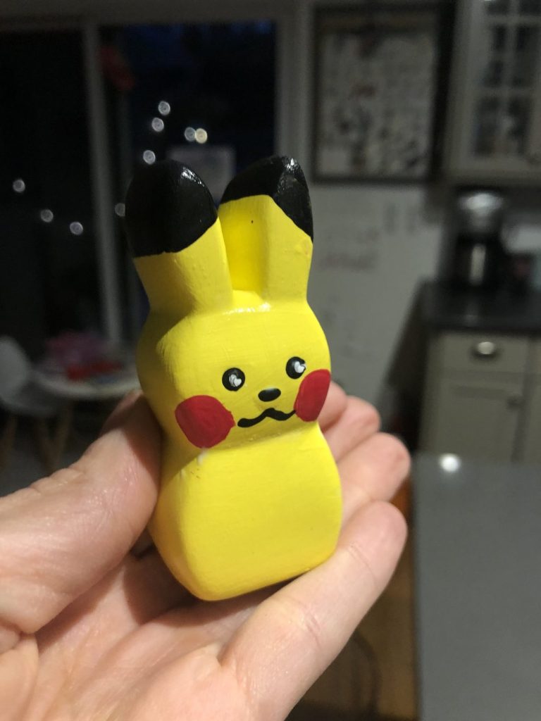 Hand holding a hand-painted yellow bunny figurine with black ear tips and red cheeks