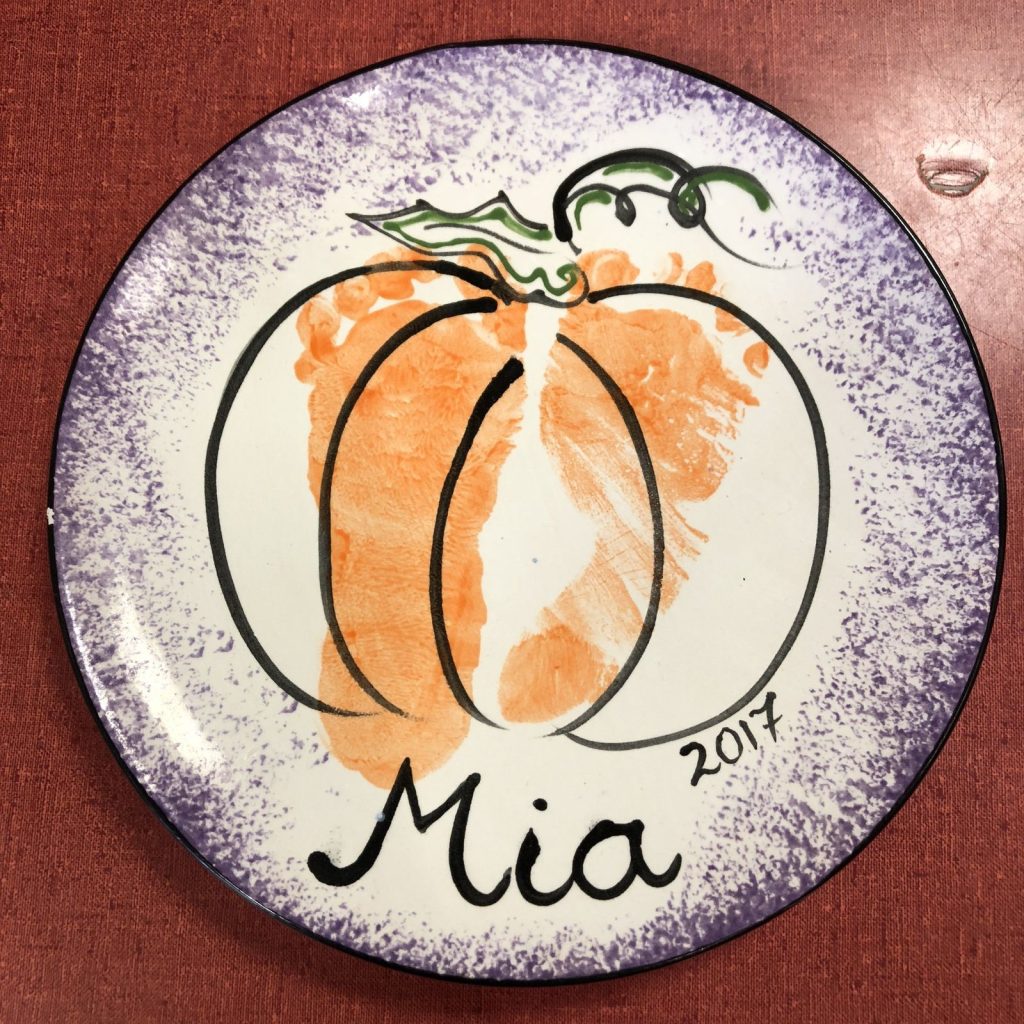 Baby footprints painted as an orange pumpkin on a round purple-speckled keepsake plate