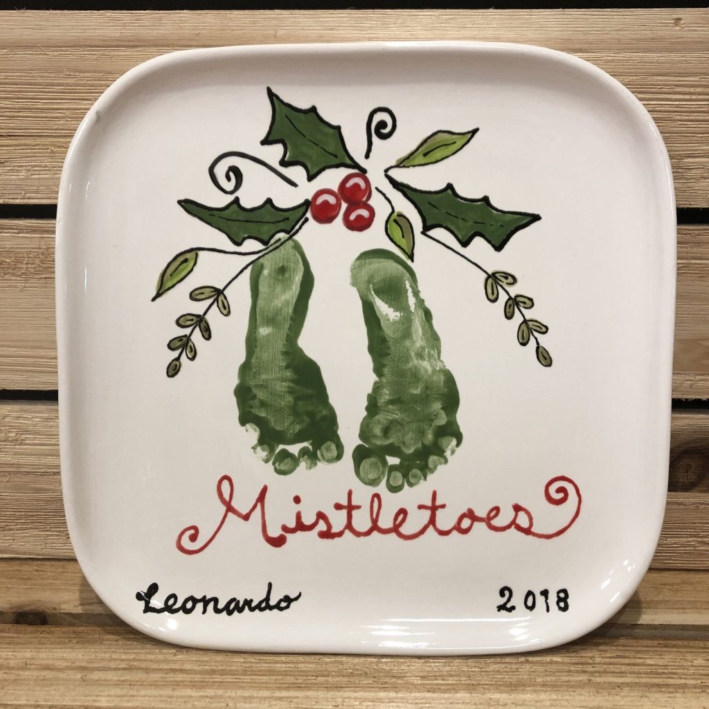 Square plate with two green baby footprints as hanging mistletoe, holly and the word Mistletoes