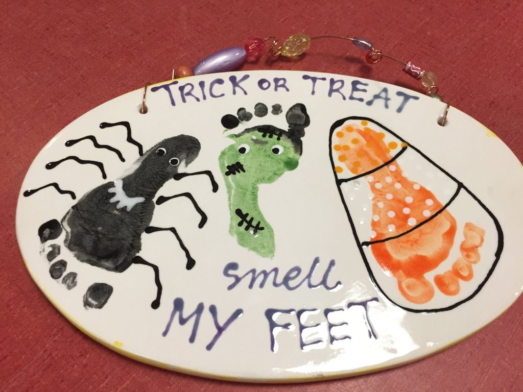 Oval Halloween plaque with footprint spider, Frankenstein and candy corn reading Smell My Feet