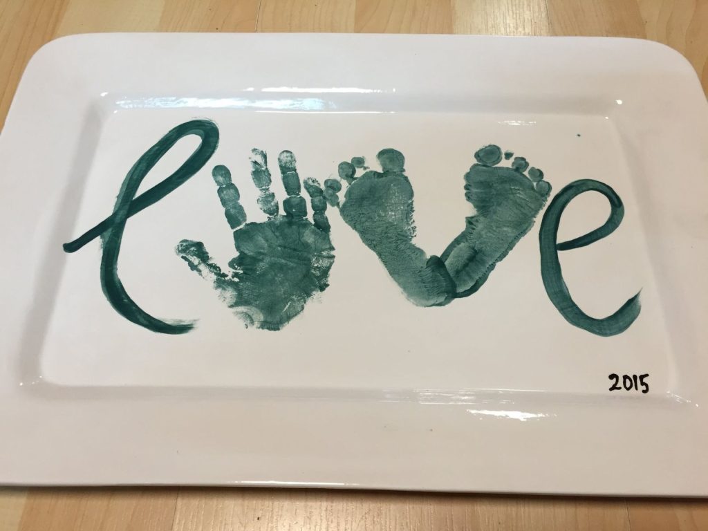 White rectangular platter with green handprint and footprints forming the word Love