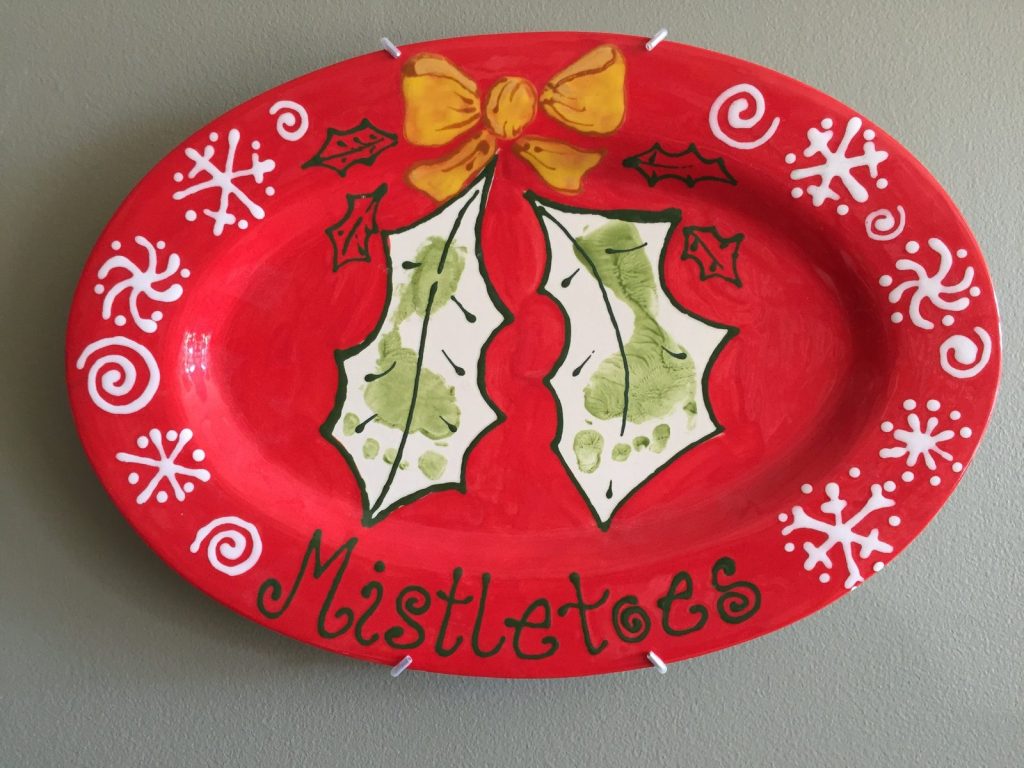 Hand-painted red oval Mistletoes platter with green footprints, a gold bow and white snowflakes