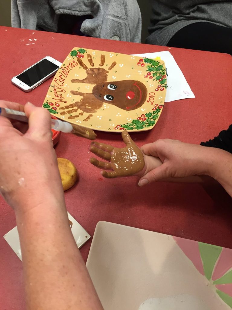 Brown paint being brushed onto a child's hand to print a reindeer plate