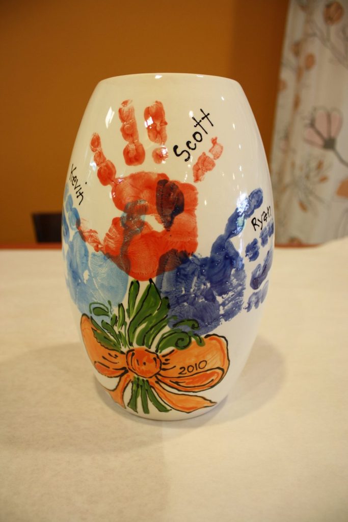 Hand-painted vase with a bouquet of colorful handprint flowers tied with an orange bow