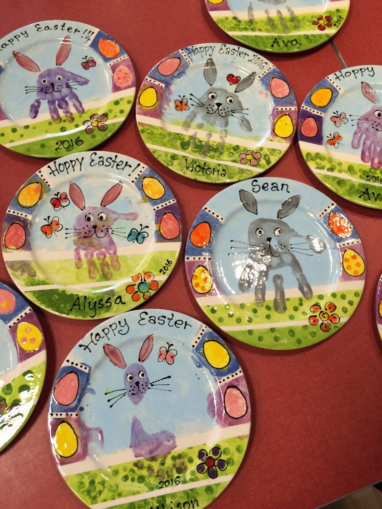 Hand-painted Happy Easter plates with handprint bunnies and colorful egg borders, shown as a group