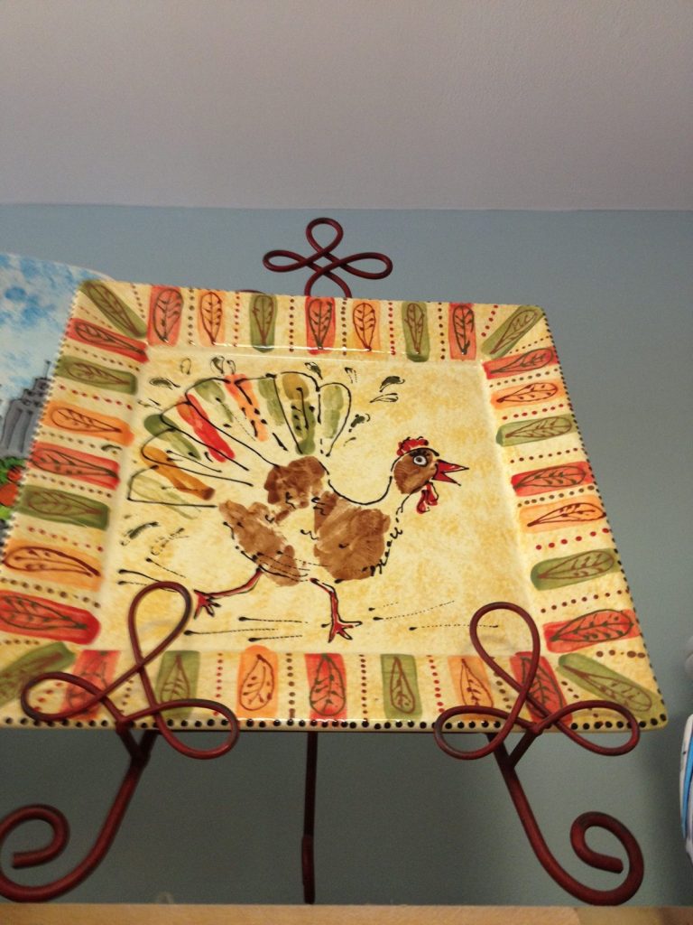 Hand-painted square platter with two handprint turkeys and a striped autumn border on a stand