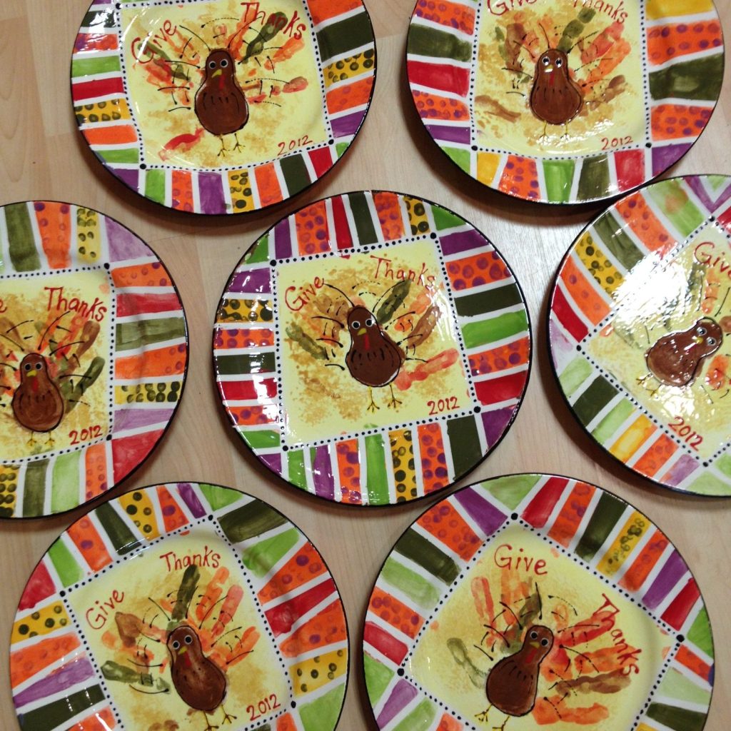 Several hand-painted Give Thanks plates with brown handprint turkeys and colorful striped borders