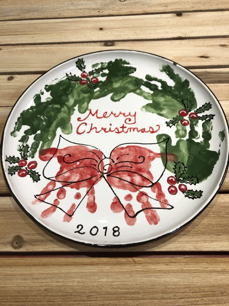 Hand-painted Merry Christmas platter with a green handprint wreath and red handprint bow, dated 2018