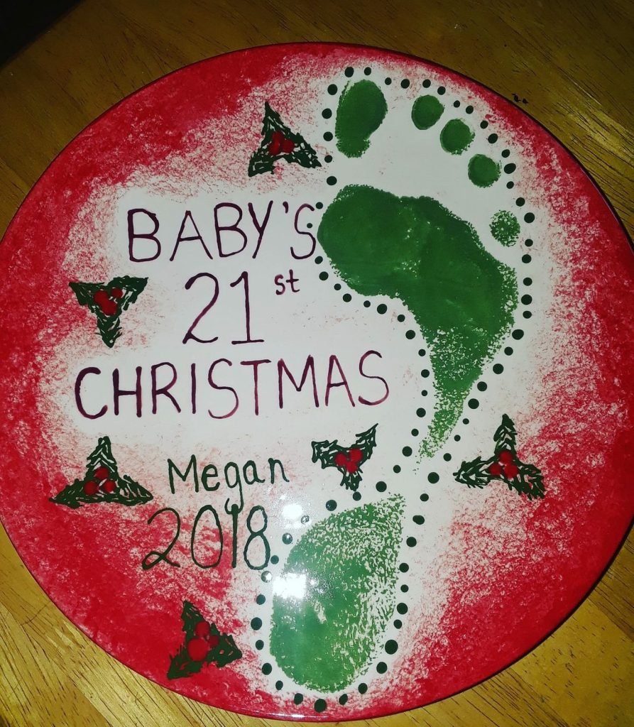 Hand-painted baby's first Christmas plate with green footprints and holly on a red speckled rim, dated 2018
