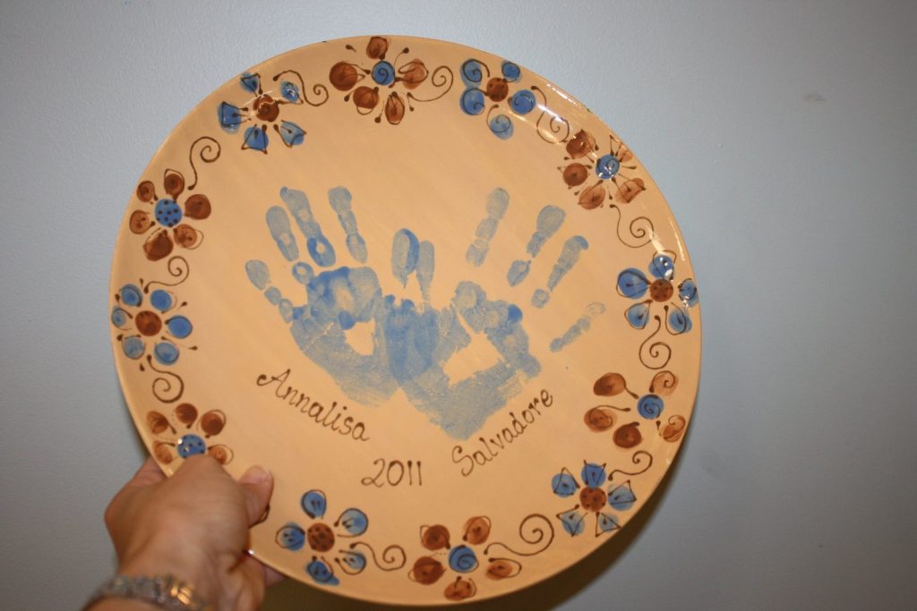 Hand-painted peach plate with two blue handprints and a blue and brown flower border, dated 2011