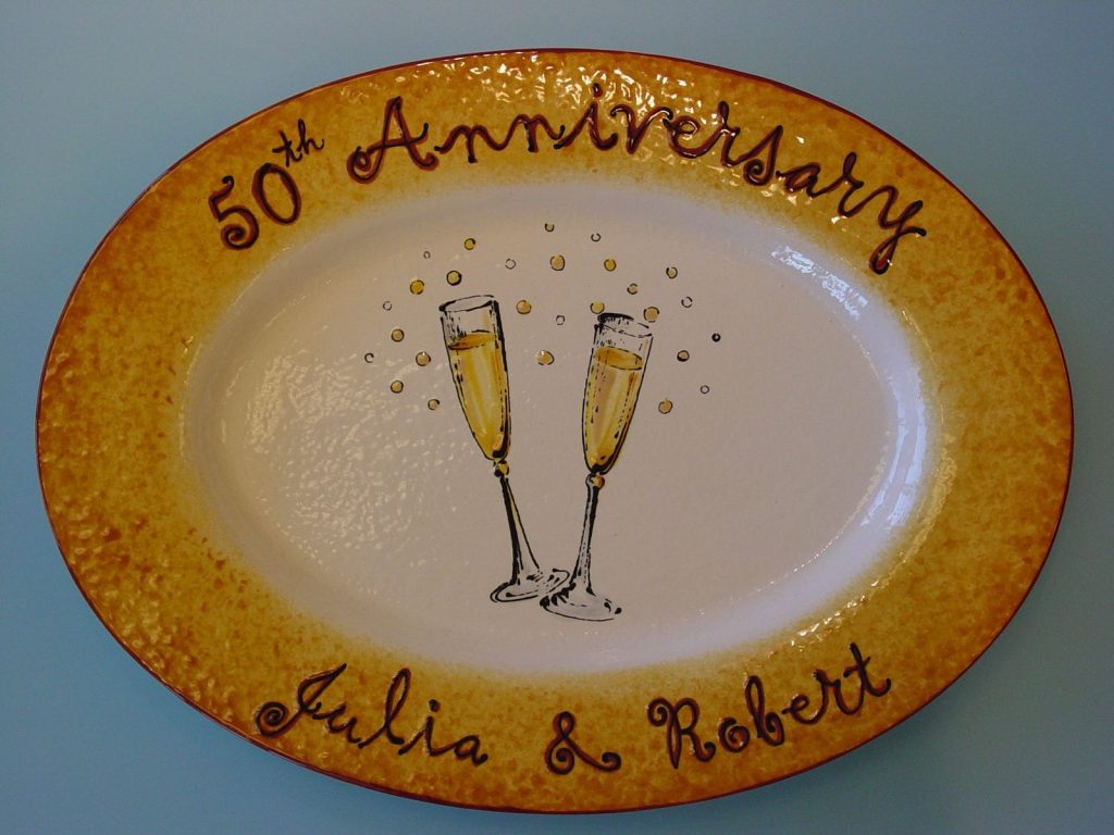 Oval 50th anniversary platter with clinking champagne flutes and a golden speckled rim, first names