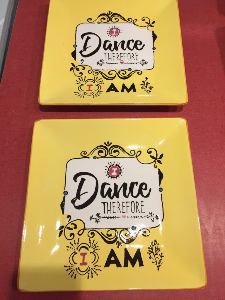 Two hand-painted yellow square plates with Dance Therefore I Am lettering in black scrollwork