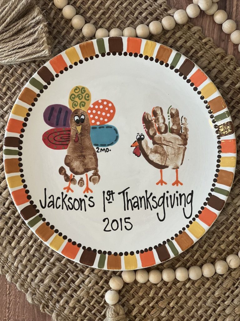 Hand-painted Thanksgiving plate with baby footprint and handprint turkeys and a striped autumn border