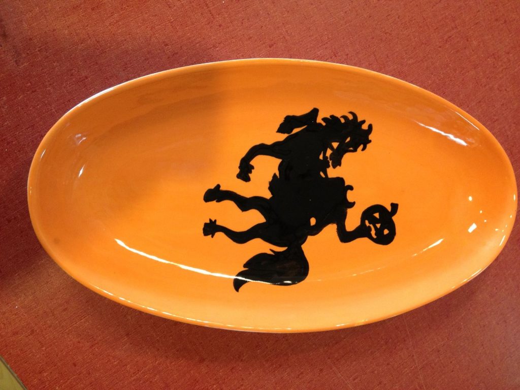 Orange hand-painted oval platter with a black silhouette of the Headless Horseman holding a jack-o-lantern