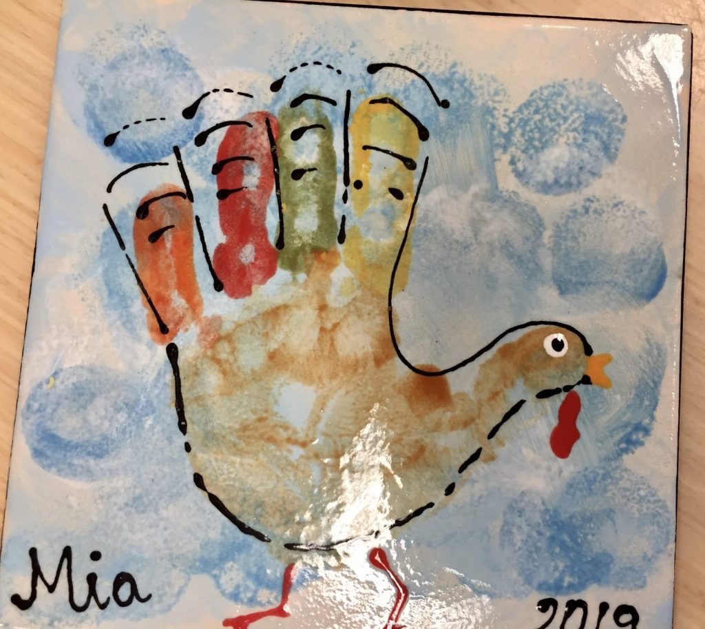 Hand-painted handprint turkey tile on a blue sponged background with the year 2019