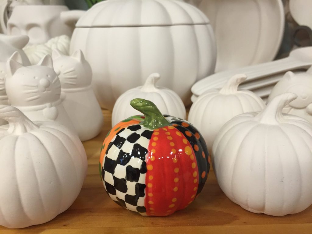 Hand-painted pumpkin in black and white checks and red stripes among unpainted white bisque pumpkins