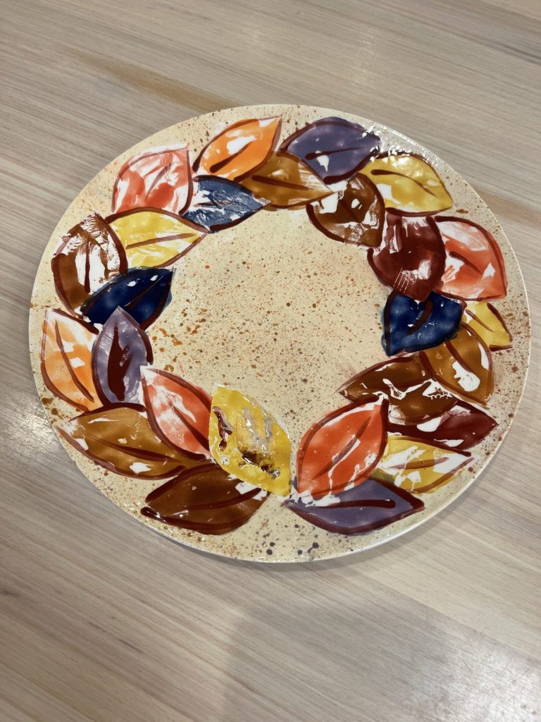 Hand-painted round plate with a wreath of multicolored autumn leaves in brown, blue, orange, and gold