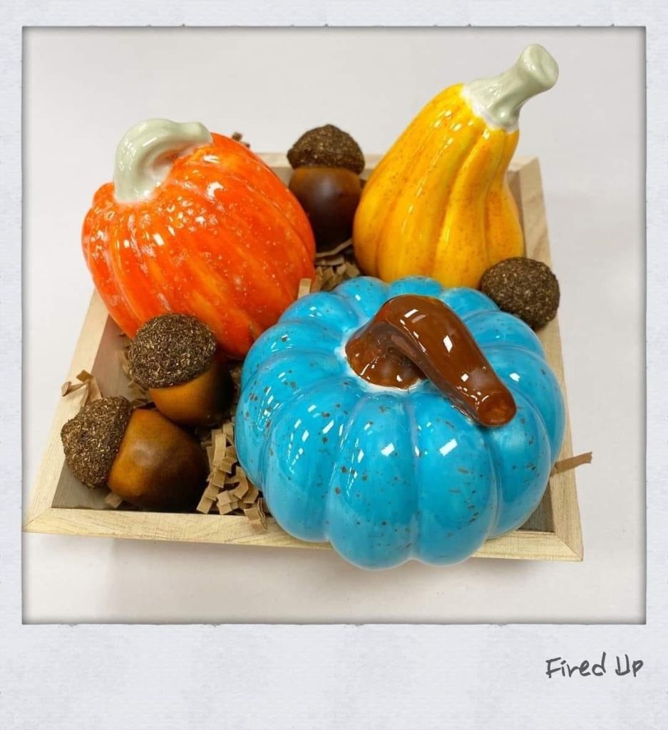 Hand-painted orange, yellow, and turquoise pumpkins and gourds with acorns in a wooden crate