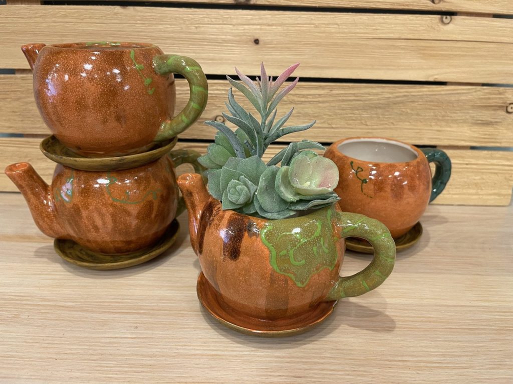 Hand-painted copper and green teapot planters with succulents alongside matching cups and a creamer