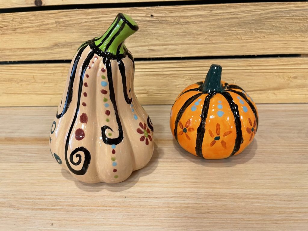 Hand-painted cream gourd with swirls and dots beside a small orange pumpkin with black stripes