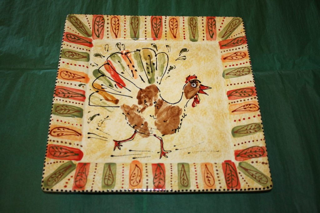 Hand-painted square platter of a handprint turkey with a colorful feather-pattern border