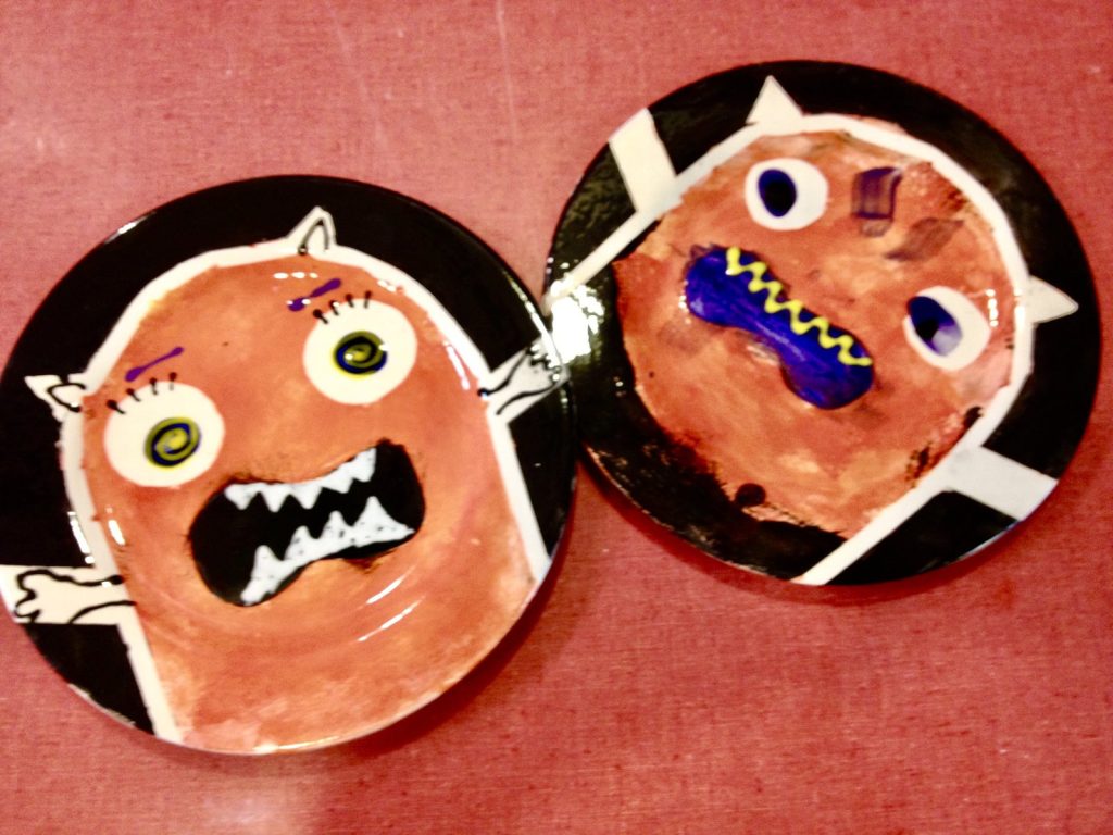 Two hand-painted monster plates with orange faces, big eyes, and toothy grins on black rims