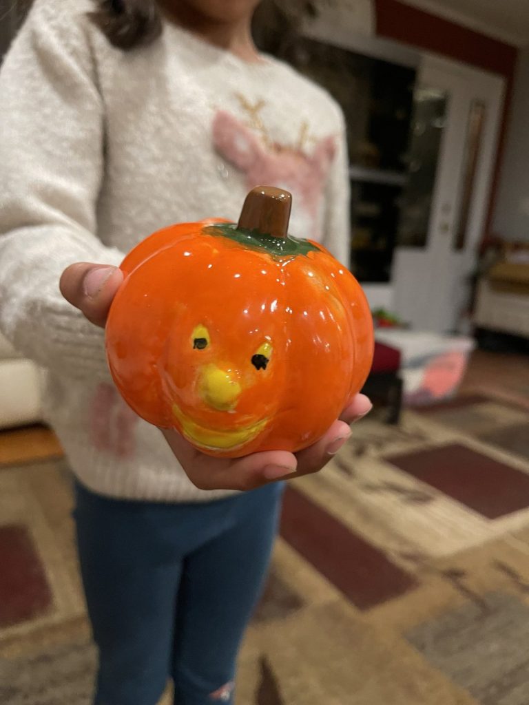 Hand-painted orange jack-o'-lantern with a smiling face held up by a child