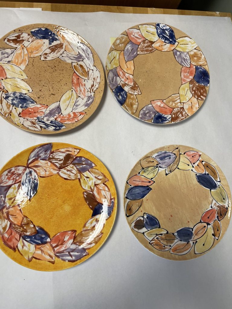 Four hand-painted plates with wreaths of multicolored autumn leaves on gold backgrounds