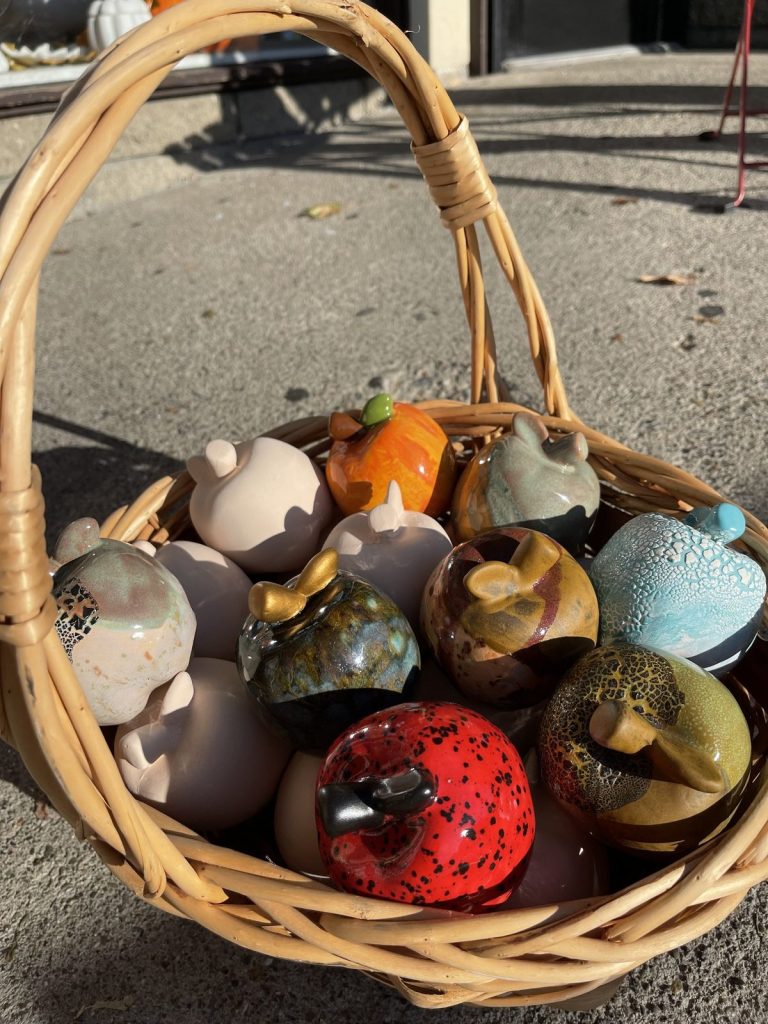 Wicker basket full of hand-painted mini pumpkins and apples in assorted glazes