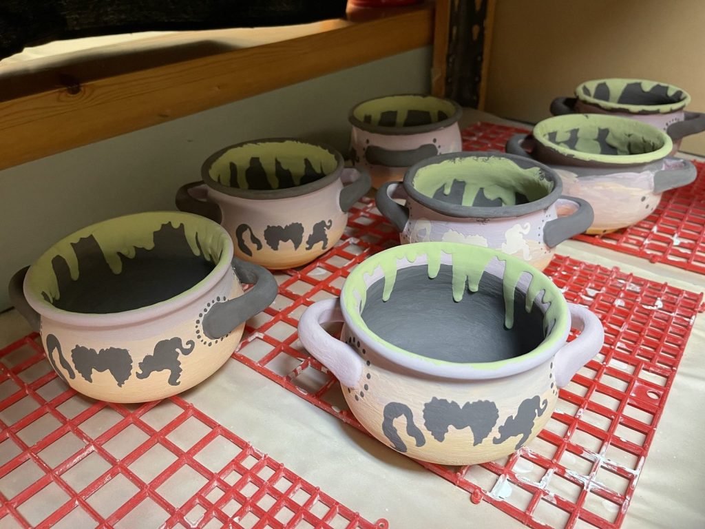 Hand-painted lavender soup crocks with green slime drips and gray ghosts on a drying rack