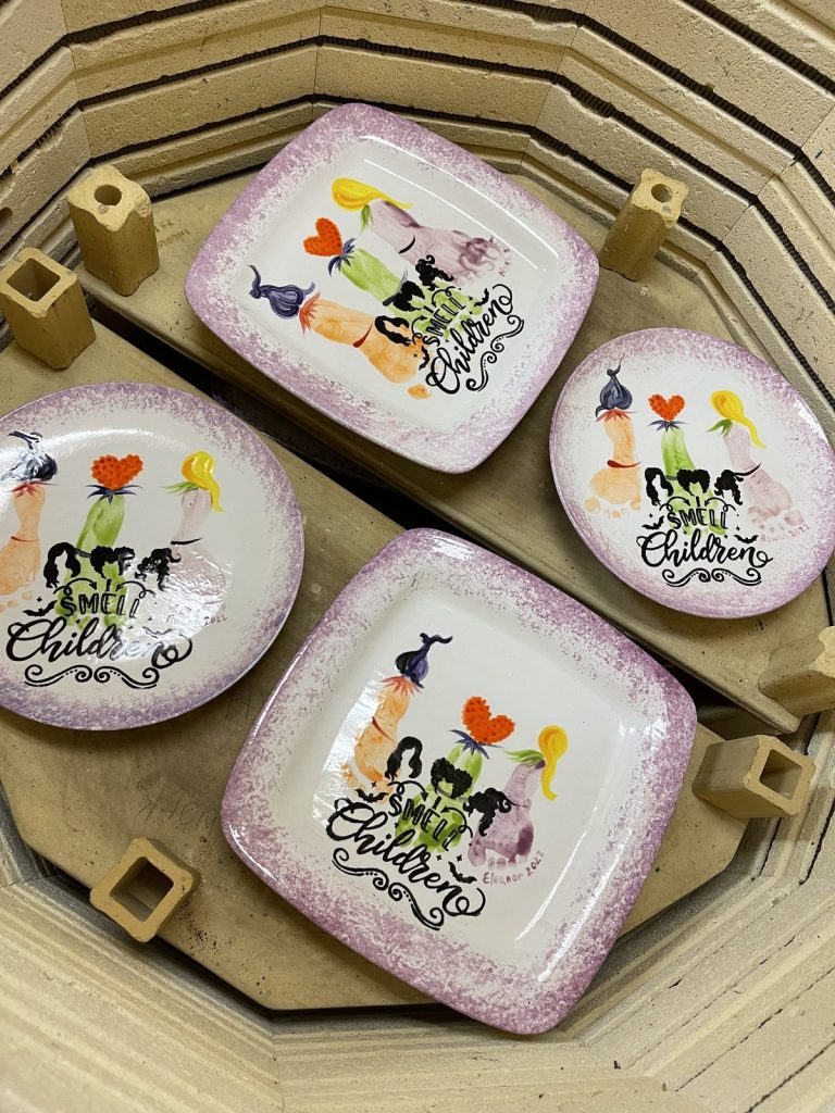 Four hand-painted footprint witch plates reading I Smell Children loaded in a kiln