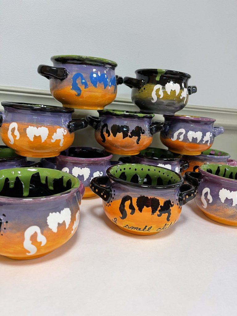 Stack of hand-painted soup crocks with orange-to-purple sunsets, slime drips, and white ghosts