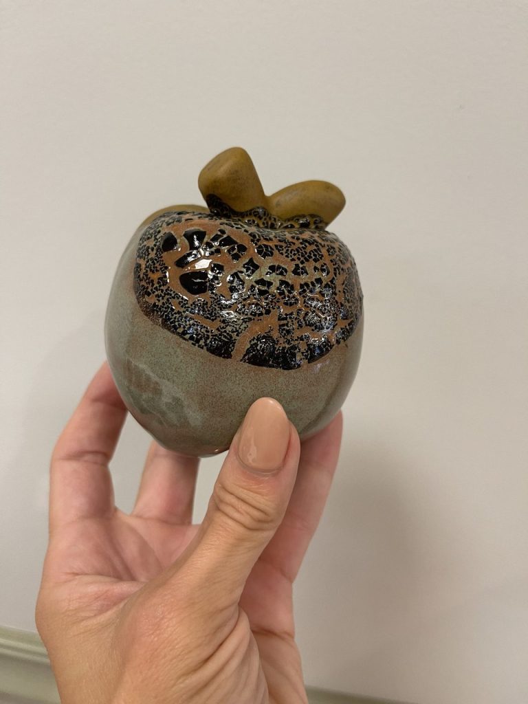 Hand-painted gray-green apple with a dark brown crackle glaze top and bronze stem